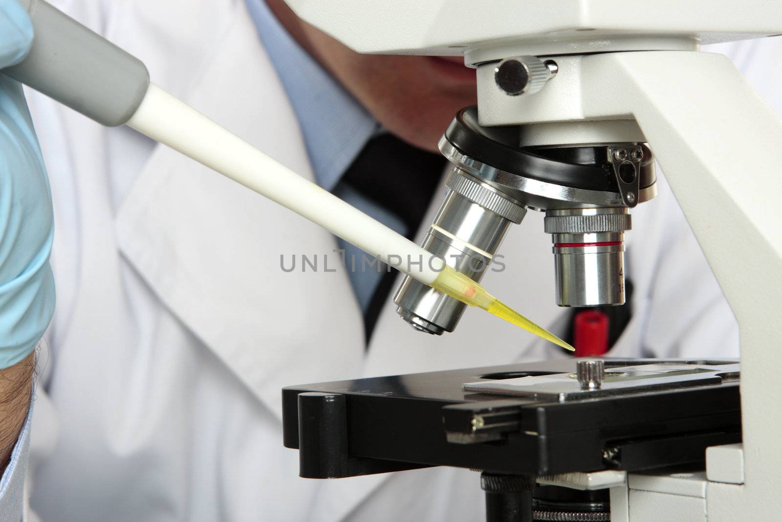 Scientist, pharmacist or chemist analyses a substance under the microsocpe.  Closeup focus to pipette tip.