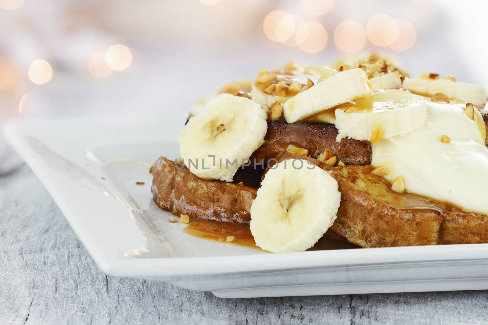 French toast topped with sliced bananas, nuts, cream cheese sauce and caramel syrup. Extreme shallow depth of field with selective focus. 