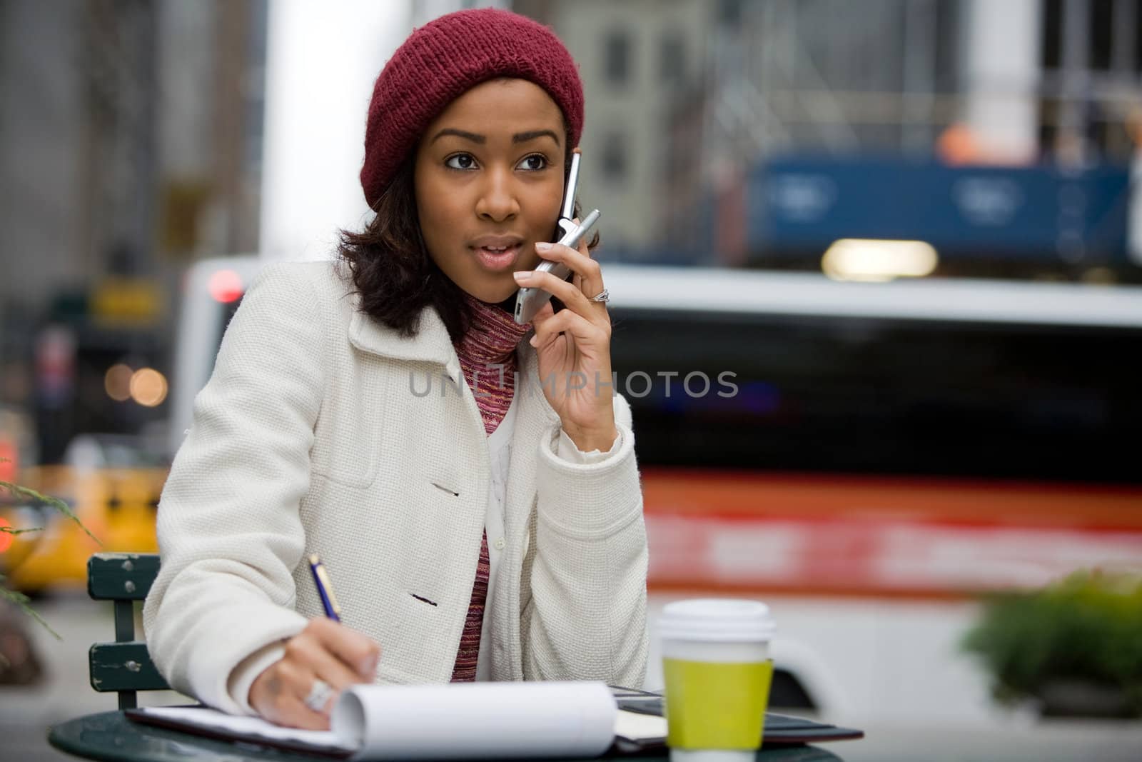 A mobile business woman in the city talks on her cell phone while writing something down in her notepad.