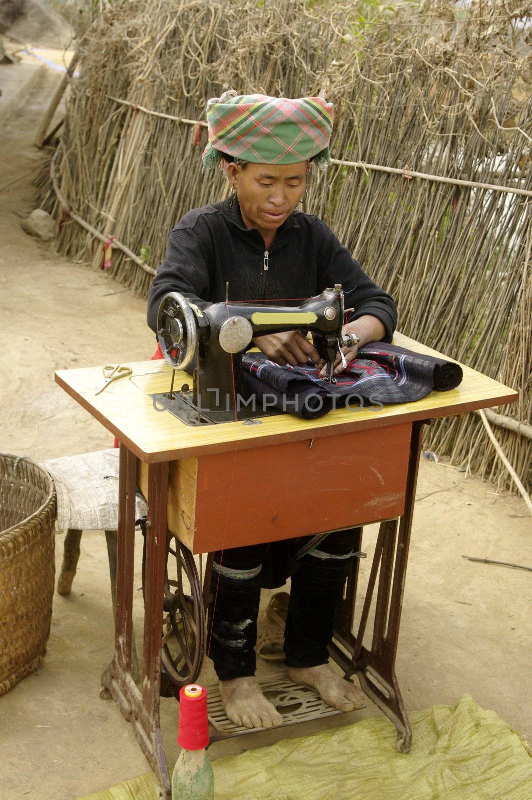 Femme ethnie Hmong noir devant sa machine à coudre .Elle est installée devant sa maison .Ses mains sont bleues de la teinture du tissus qu’elle coud .Cette machine est l’unique fortune du couple .