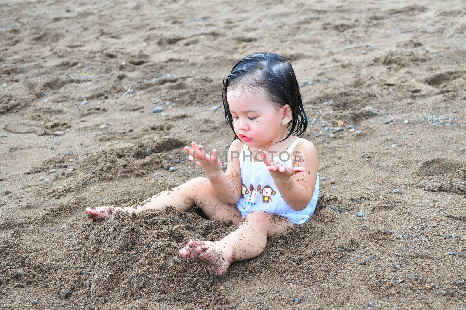 Cute little girl playing with sand for the first time at the beach.
