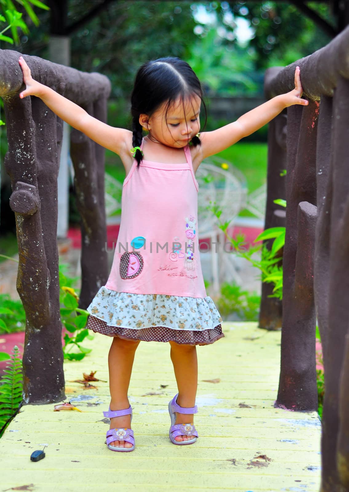 A little girl standing on a bridge with arms spread wide open.