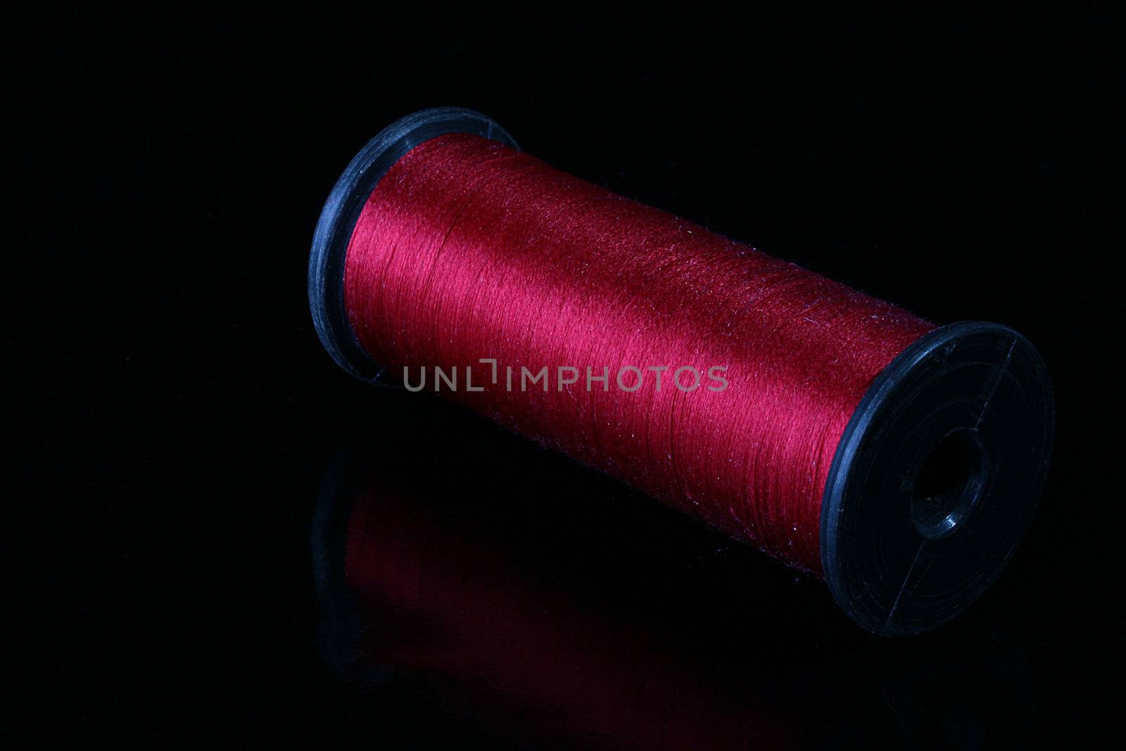 Darkly red threads on the coil for industrial use. Threads are placed on a black reflecting background.