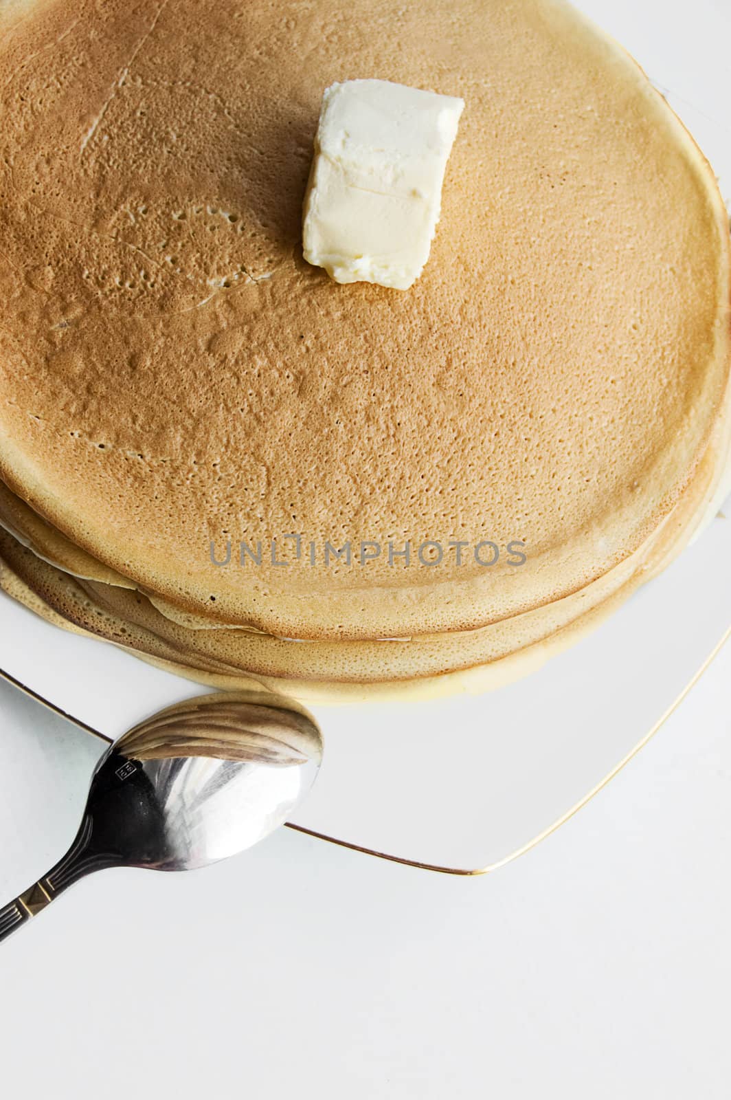 Pile of pancakes with butter and spon on plate
