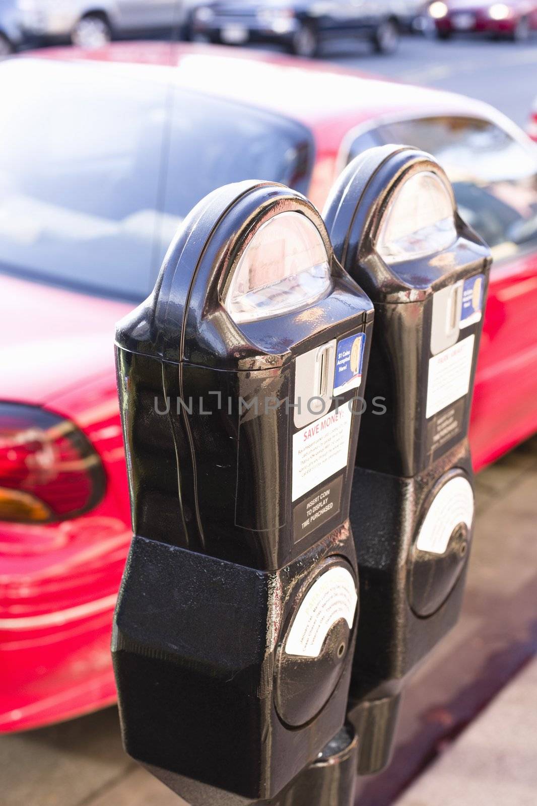 Closeup of Two Parking Meters in Front of a Parked  Red Car