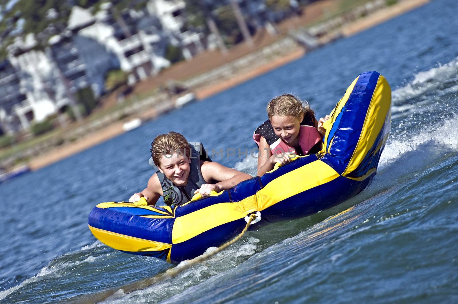 Young boy and girl on a tube behind a boat.