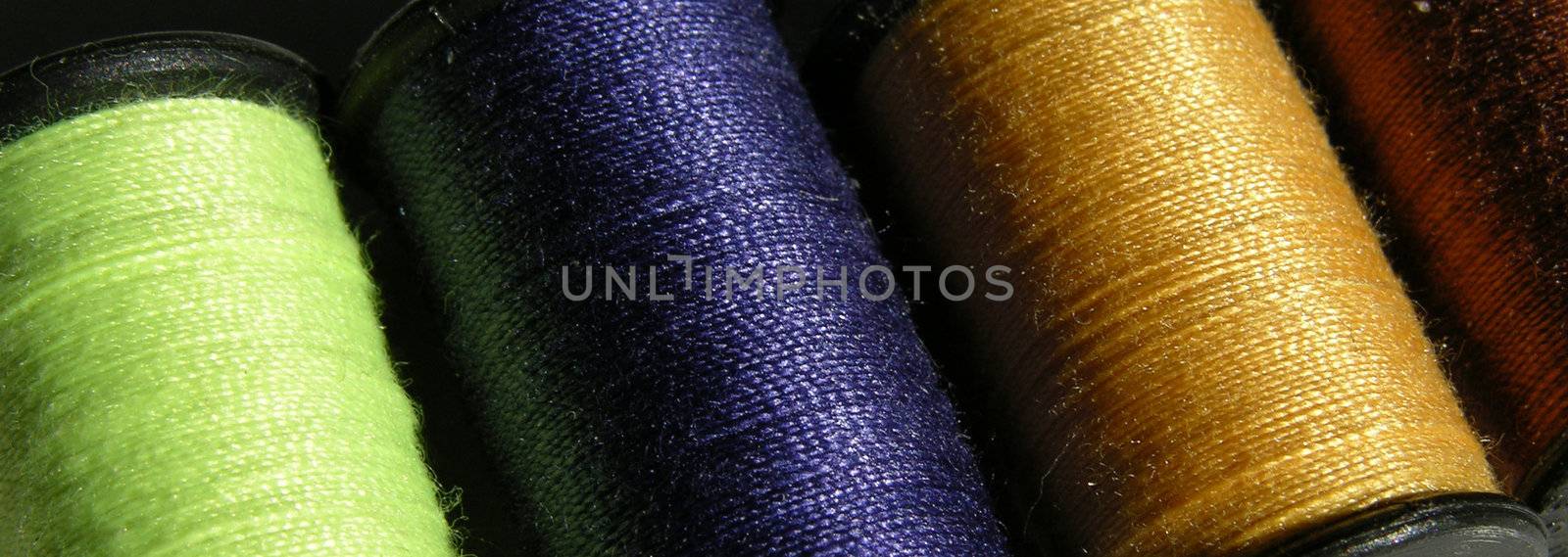 Four spools of thread seen closeup in different colors