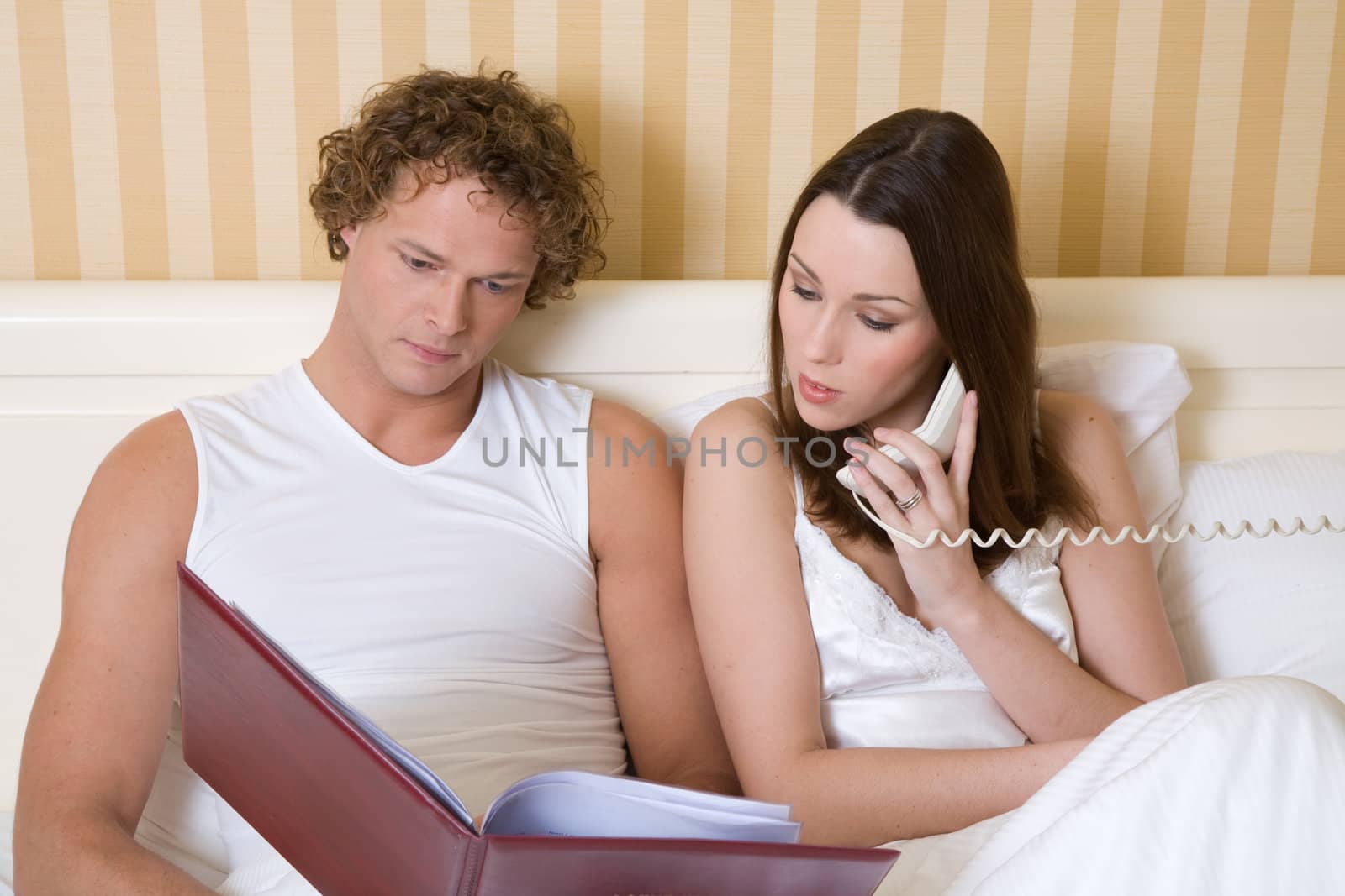 Young couple sitting together in hotel bed with roomservice menu