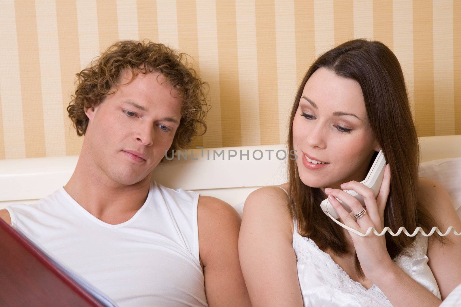 Couple in bed checking the menu and calling roomservice