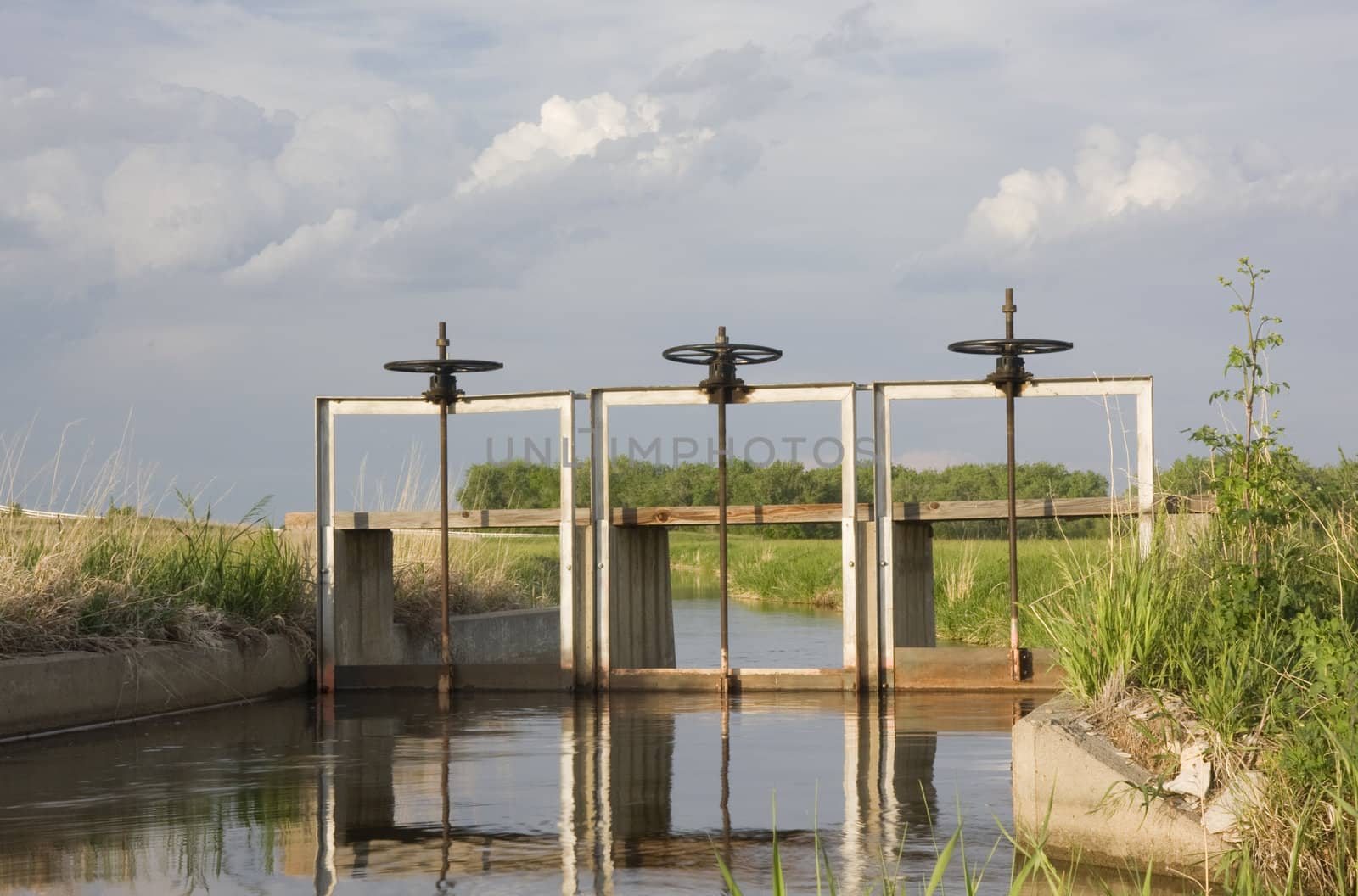 full of water irrigation ditch with three headgates by PixelsAway