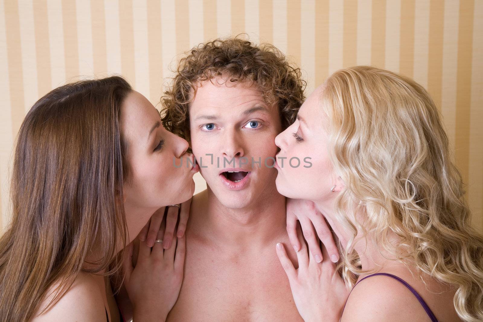 Handsome male getting a kiss from two beautiful women