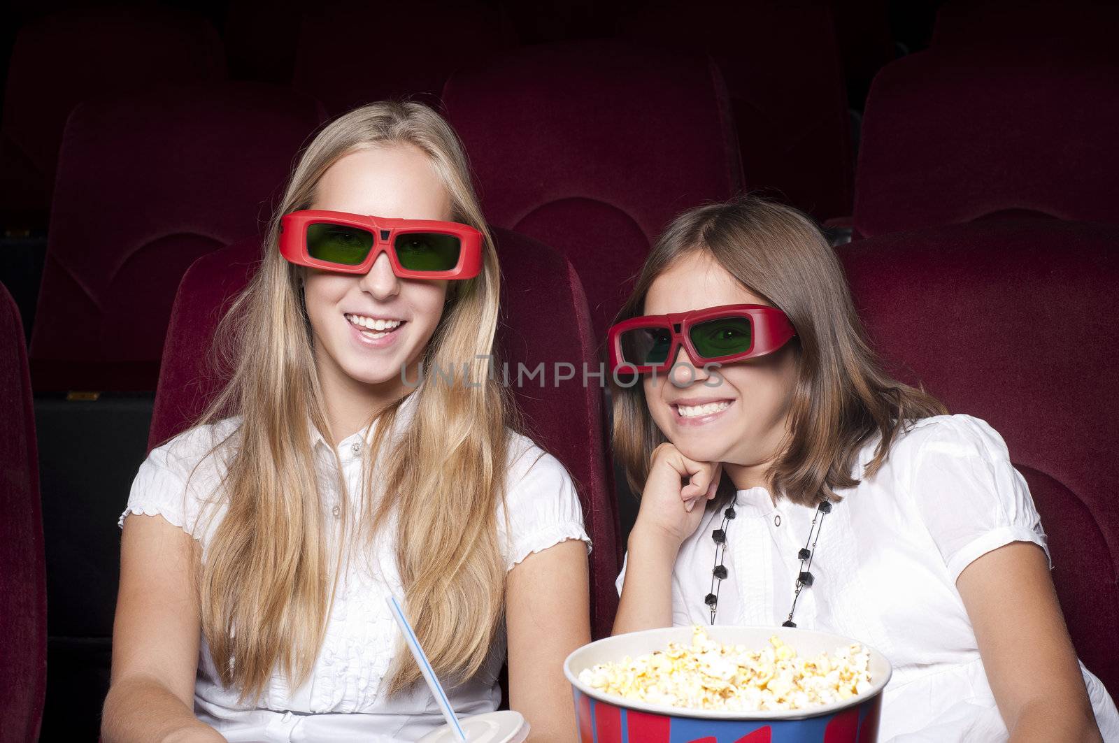 two girls look three-dimensional cinema, sitting in the glasses, eat popcorn, drink drink
