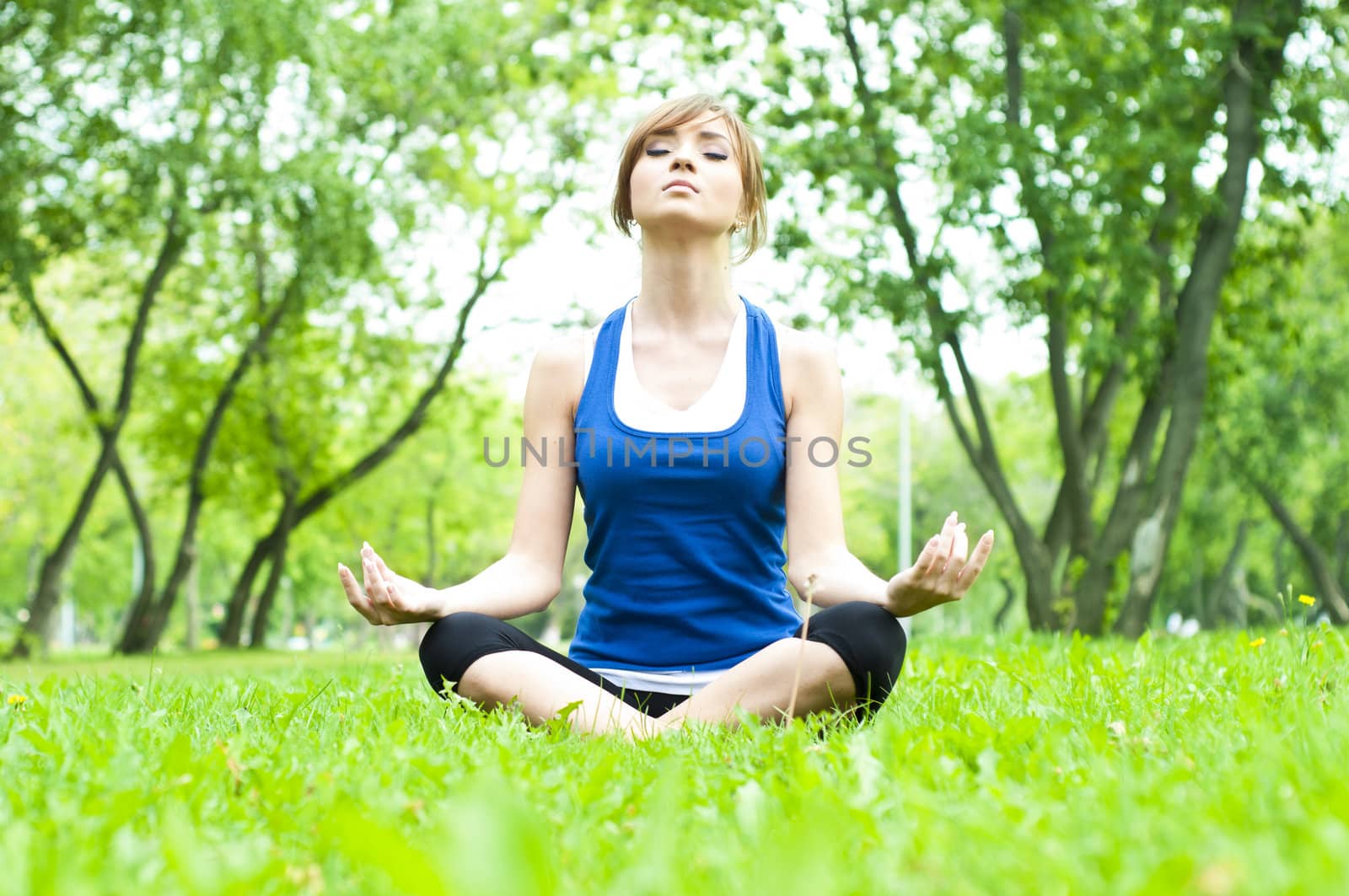 young woman is engaged in yoga, in summer forest on a green grass