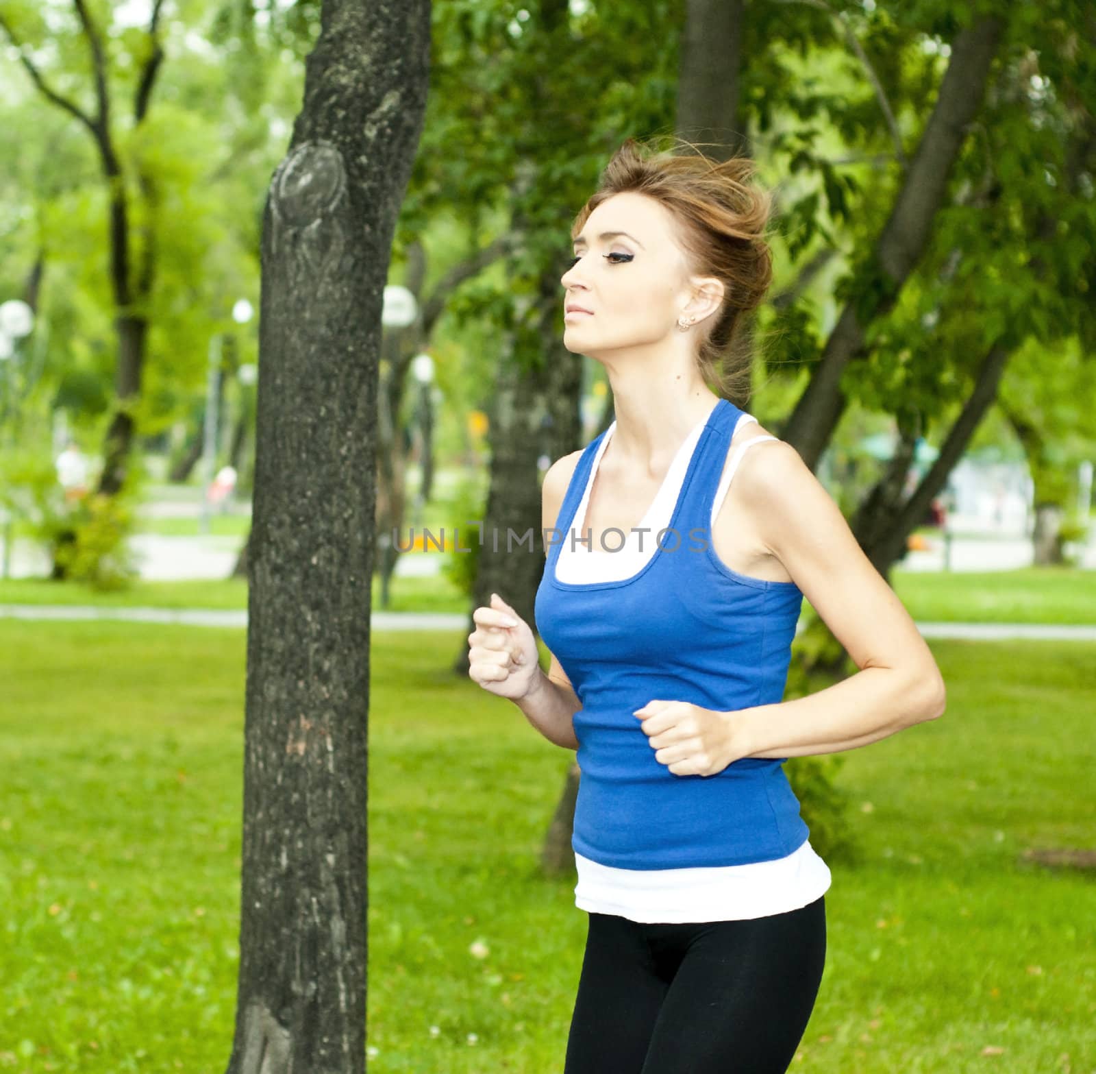 young woman jogging in the park in summer, trees and grass background
