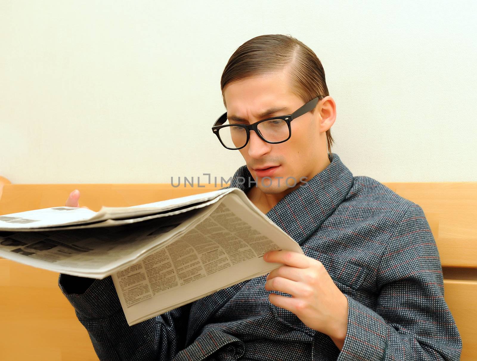 Young handsome man in dressing gown and glasses reads newspaper