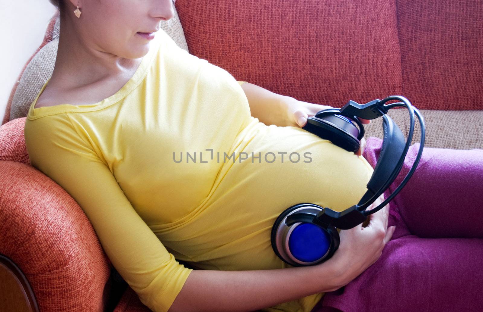 Pregnant woman with headphones on her belly lying on sofa