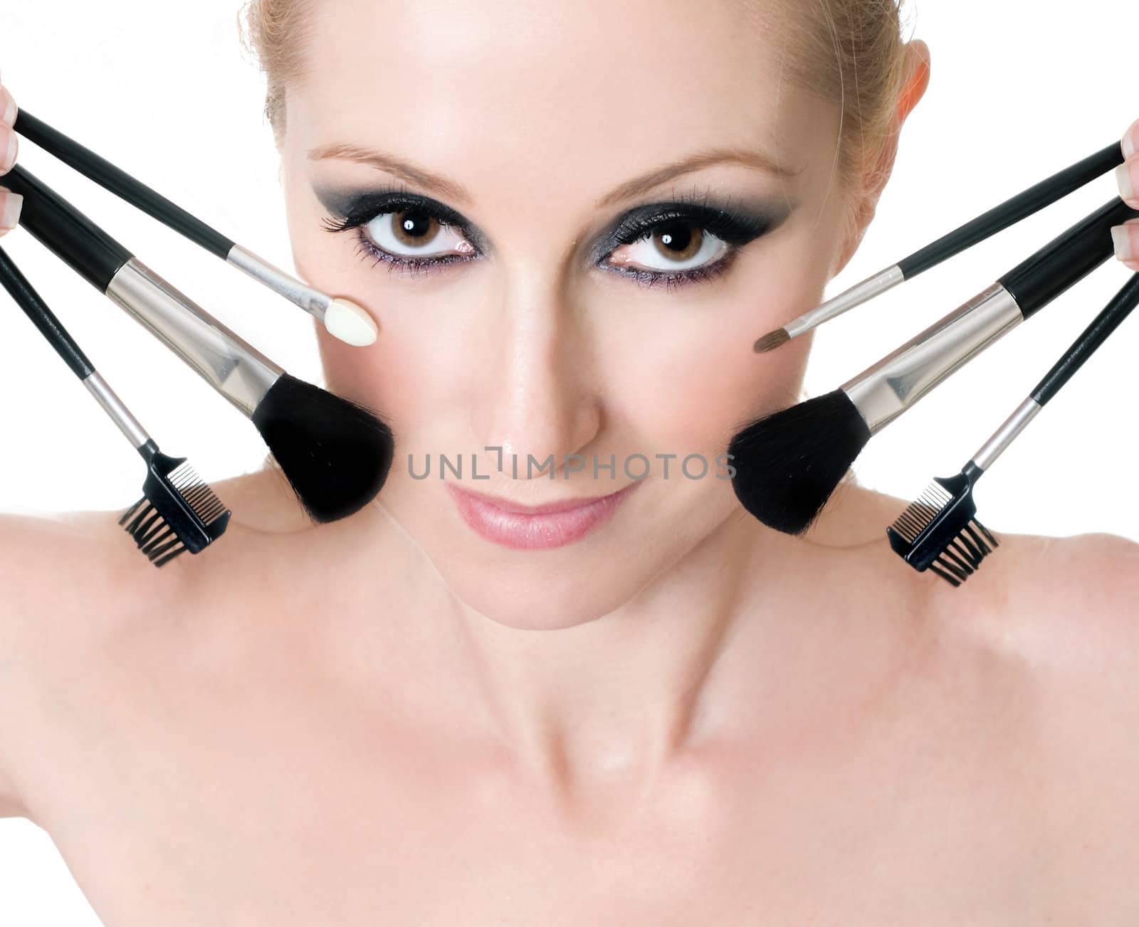 Makeup brushes and tools help achieve flawless application of cosmetics.  Brushes and applicators surround a woman's face.