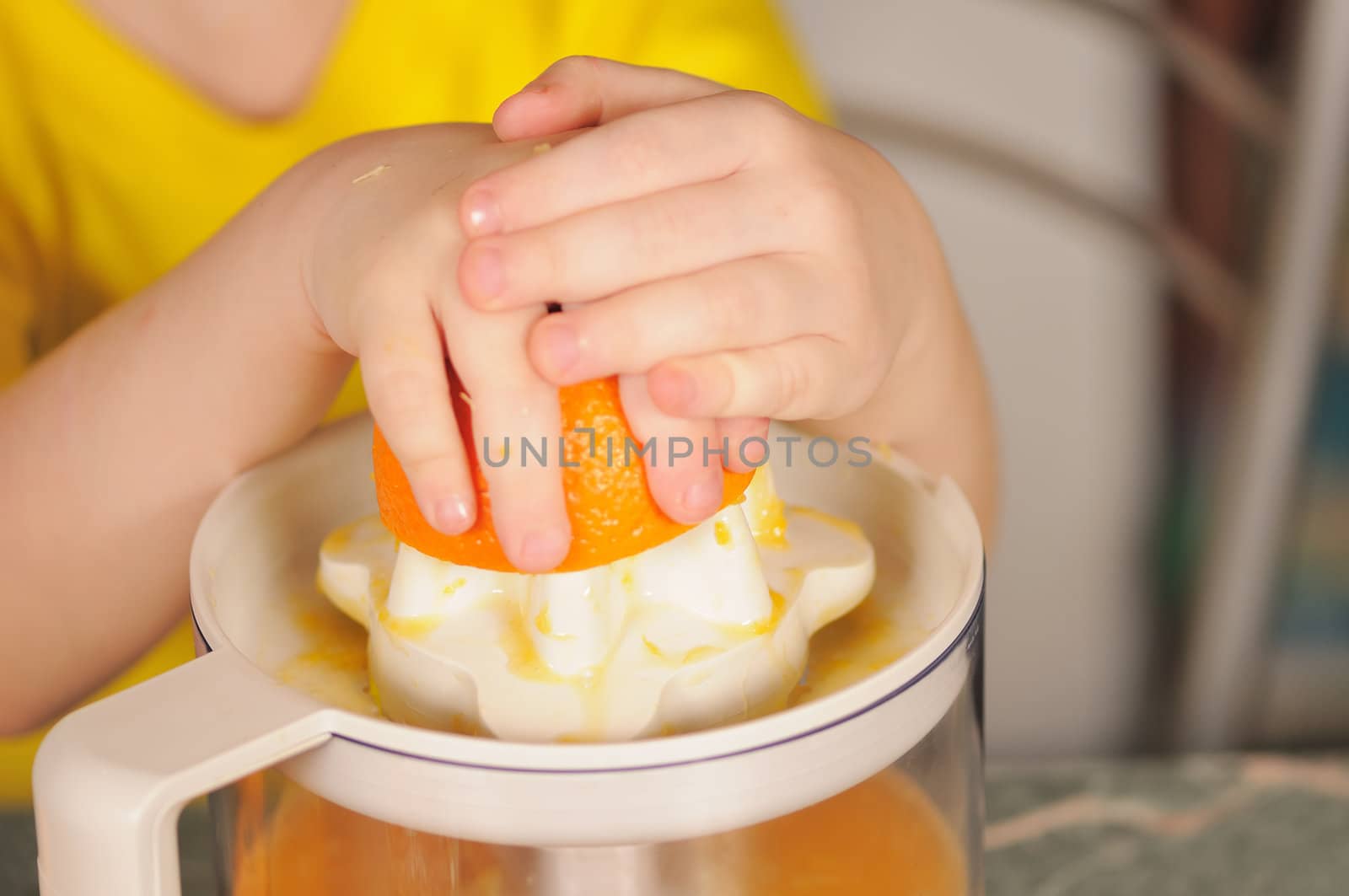 The child in a yellow vest to wring out juice  from an orange