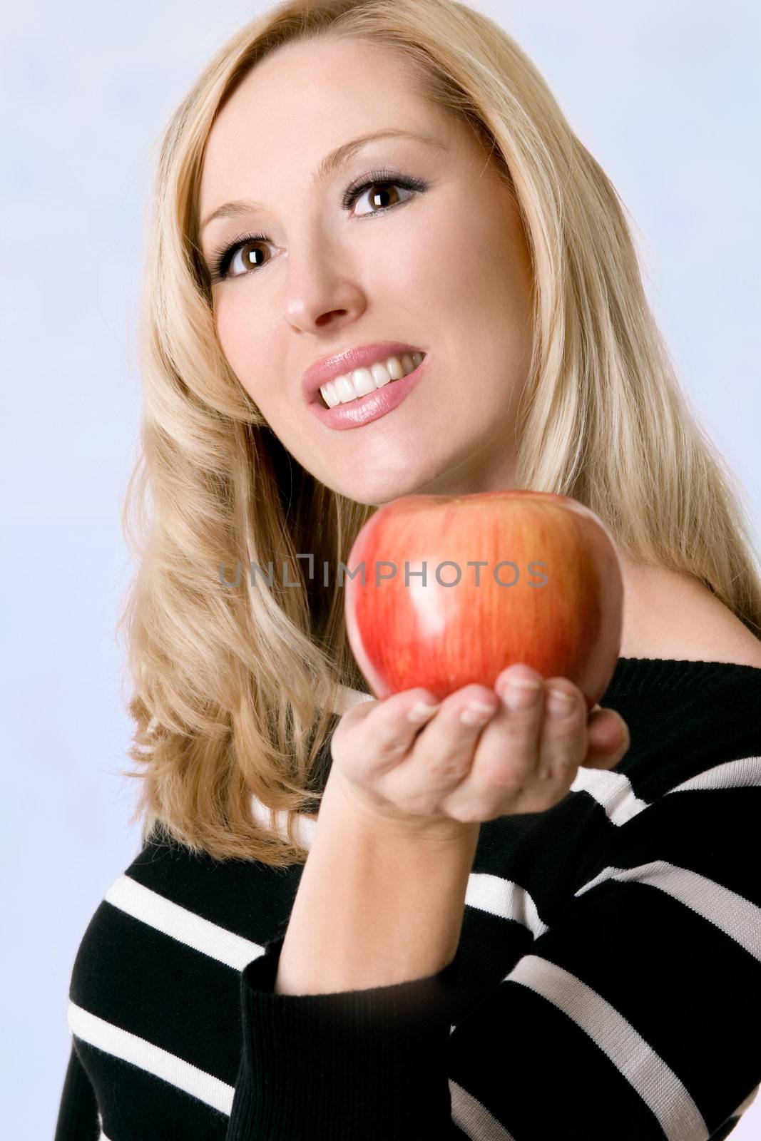 Smiling attractibe female with blonde hair holding a juicy red apple in the palm of her hand.