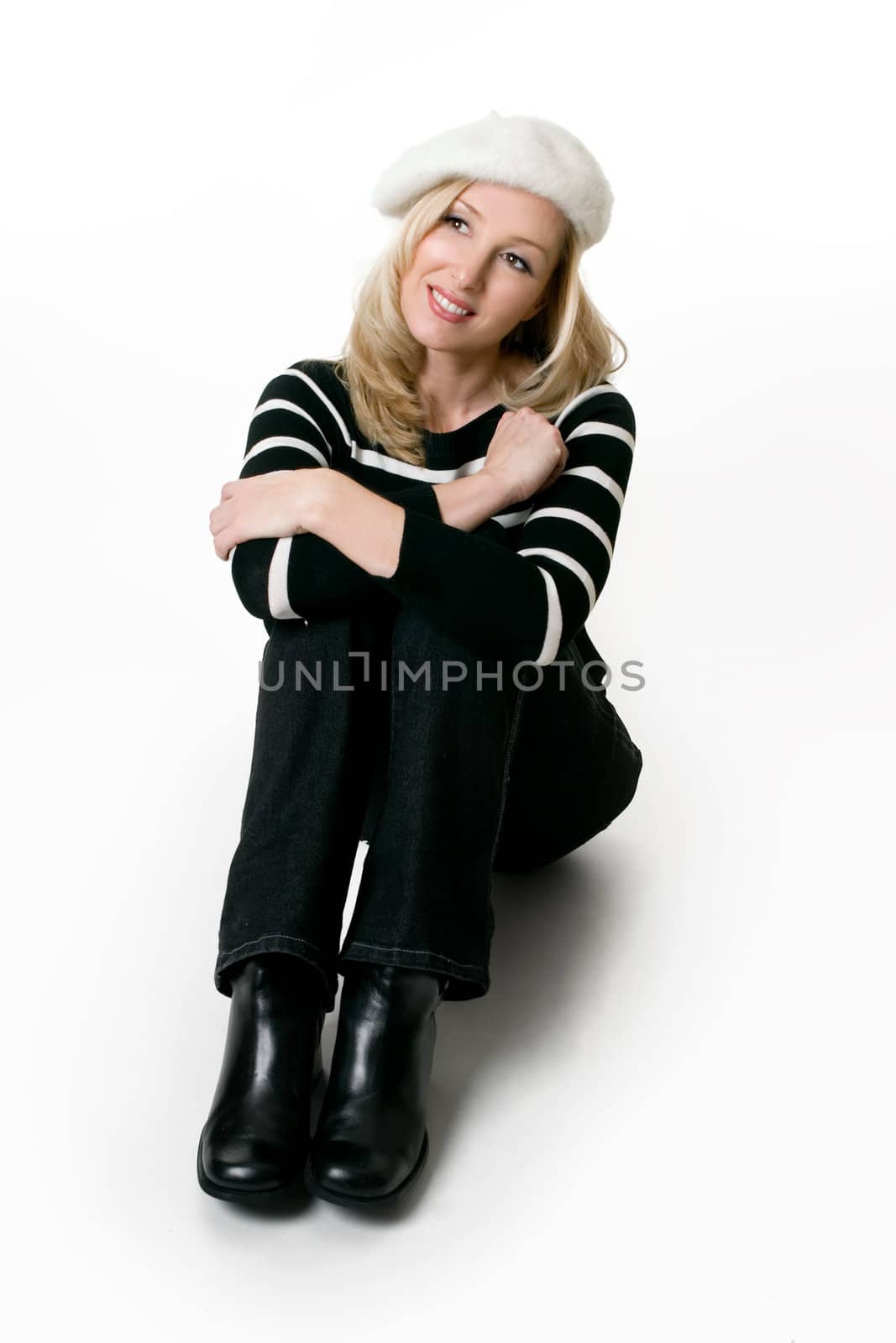 Relaxed casual woman wearing black jeans, black leather boots and black and white sweater sitting on a white background.