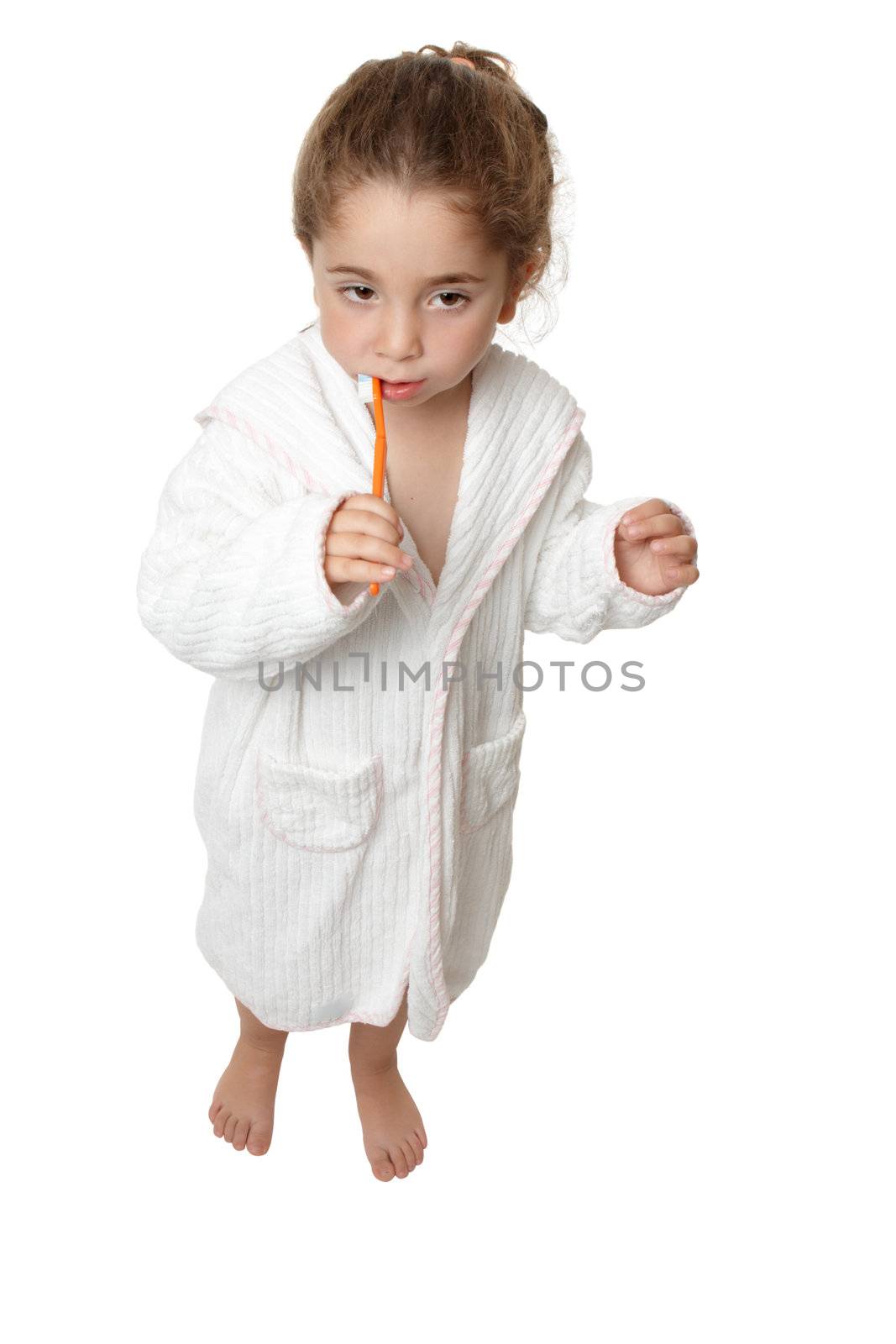 A small toddler girl in bathrobe is standing and brushing her teeth