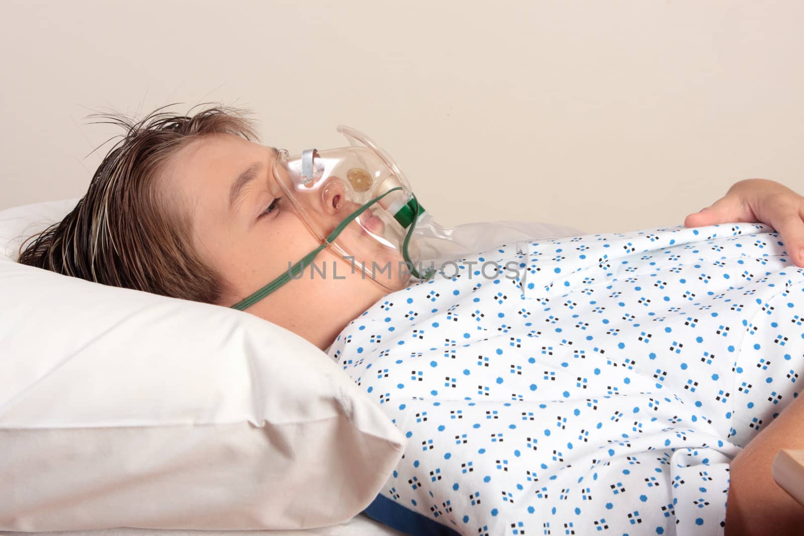 A child resting on a bed wearing patient gown has an oxygen mask or inhaler over face.