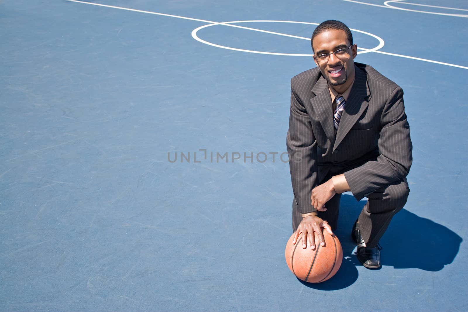 A young man in a business suit posing in the empty basketball court with lots of copyspace.