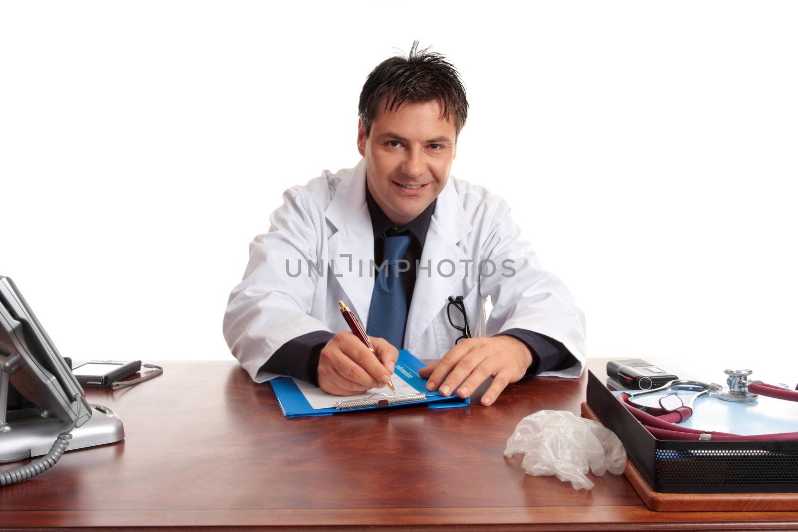 Medical doctor sitting at desk writing with pen on a  medical form.  He is looking up and smiling and listening.