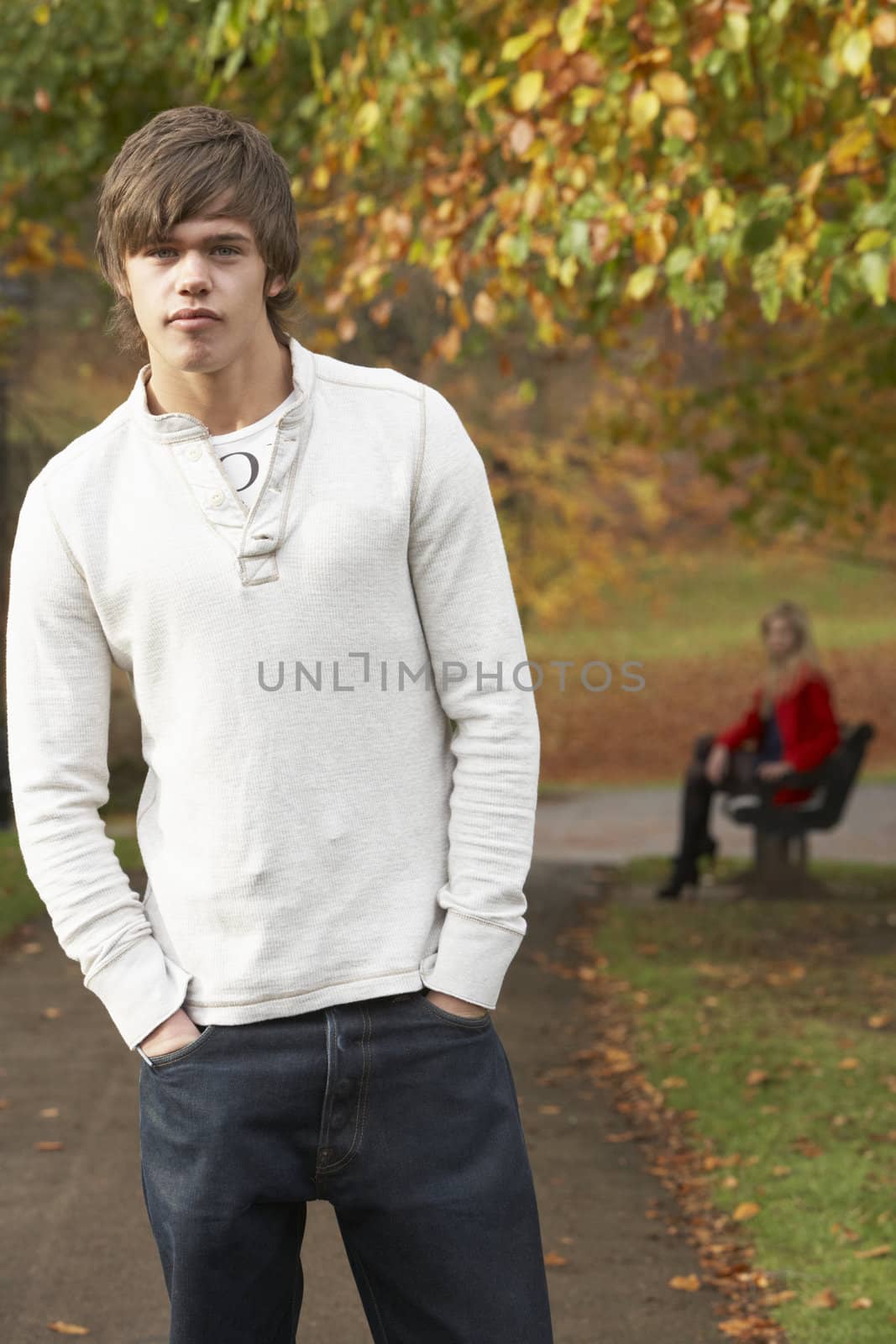Teenage Boy Standing In Autumn Park With Female Figure On Bench  by omg_images