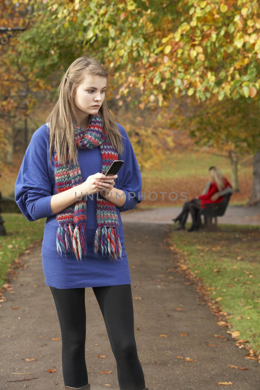 Unhappy Teenage Girl Standing In Autumn Park With Couple On Benc by omg_images