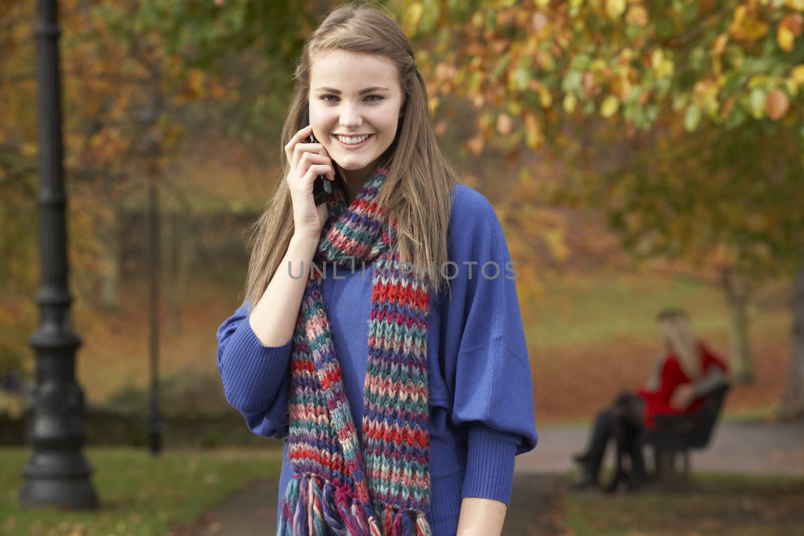 Teenage Girl On Mobile Phone In Autumn Park With Couple On Bench by omg_images