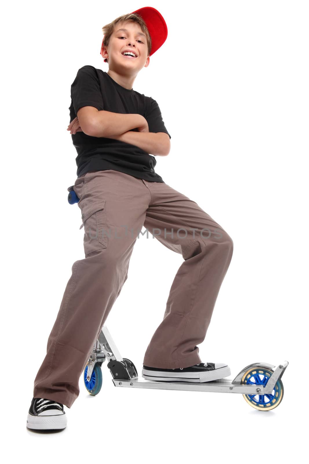 Low angle view of a relaxed boy sitting on the handlebars of a scooter.  He has his feet apart, arms crossed and is smiling in a friendly manner.