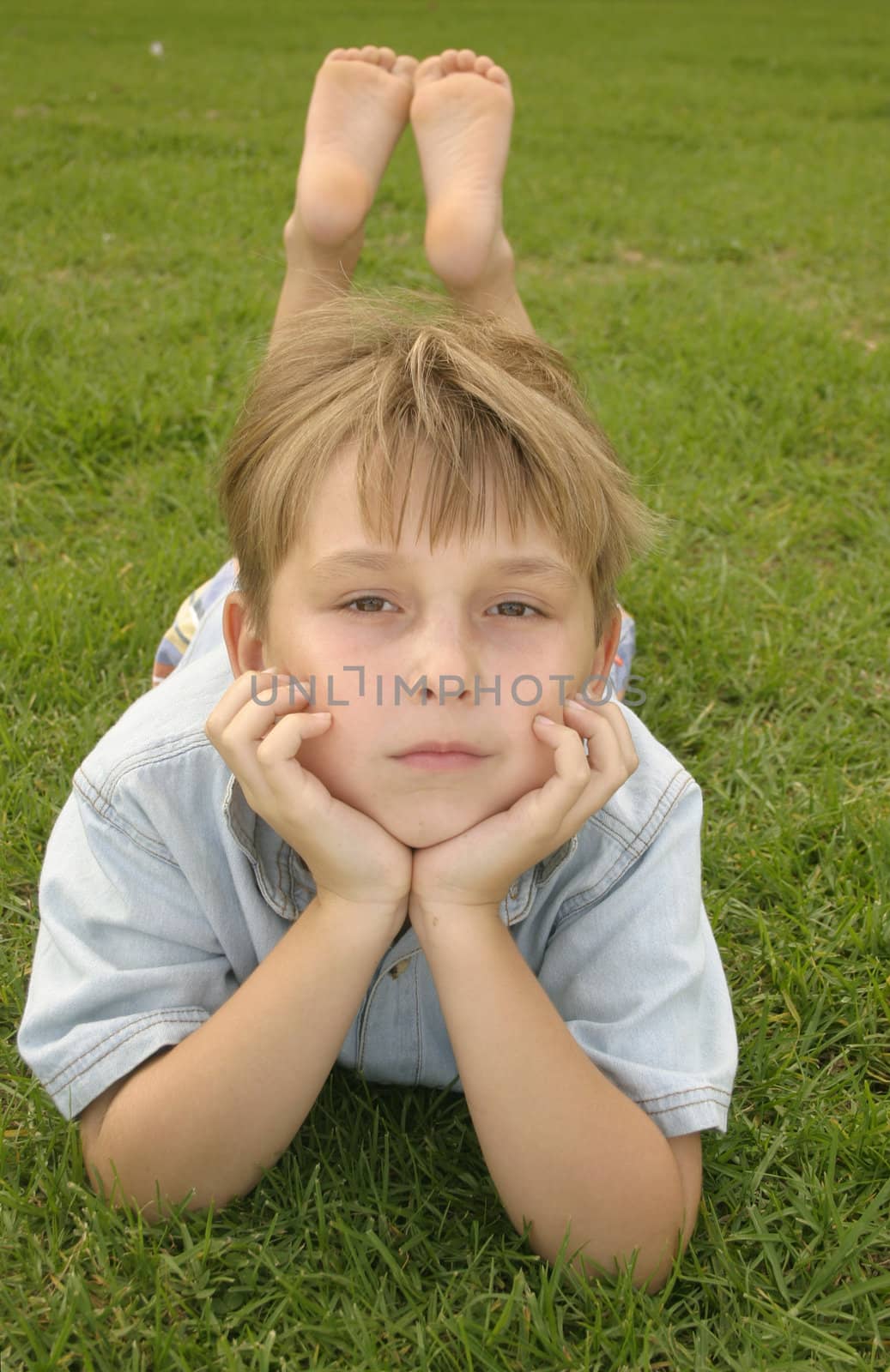 child laying on stomach on lush green parklands. 