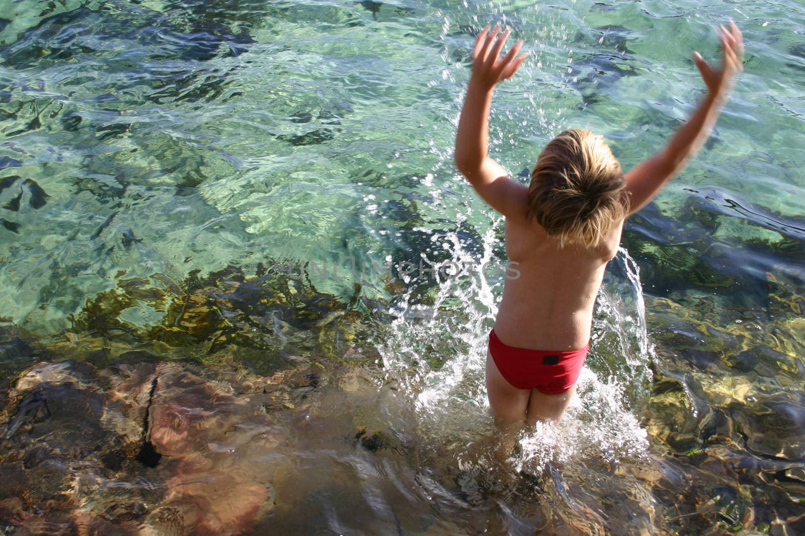 Boy splashes water overhead from an ocean rockpool.   
Somet motion blur in the hands.
