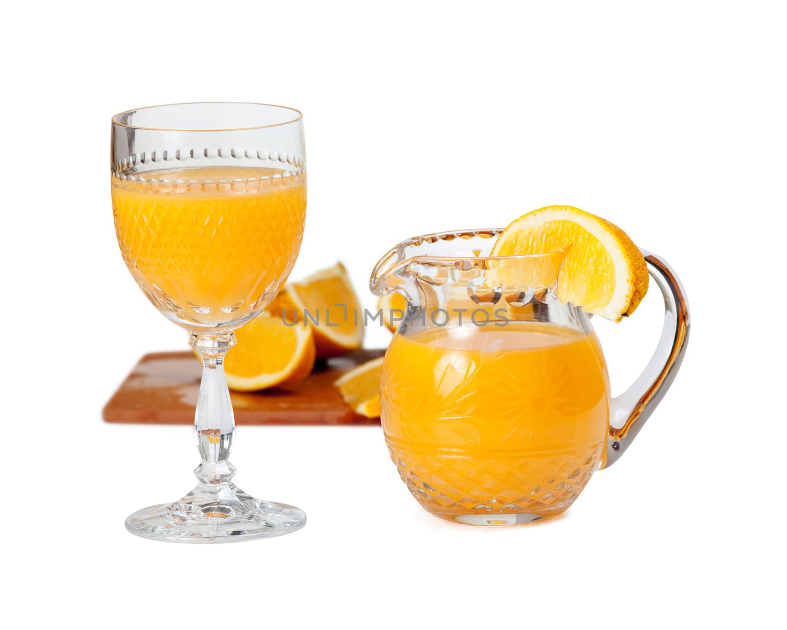 Cut glass isolated goblet and jug filled with fresh orange juice with orange slice on edge of jug
