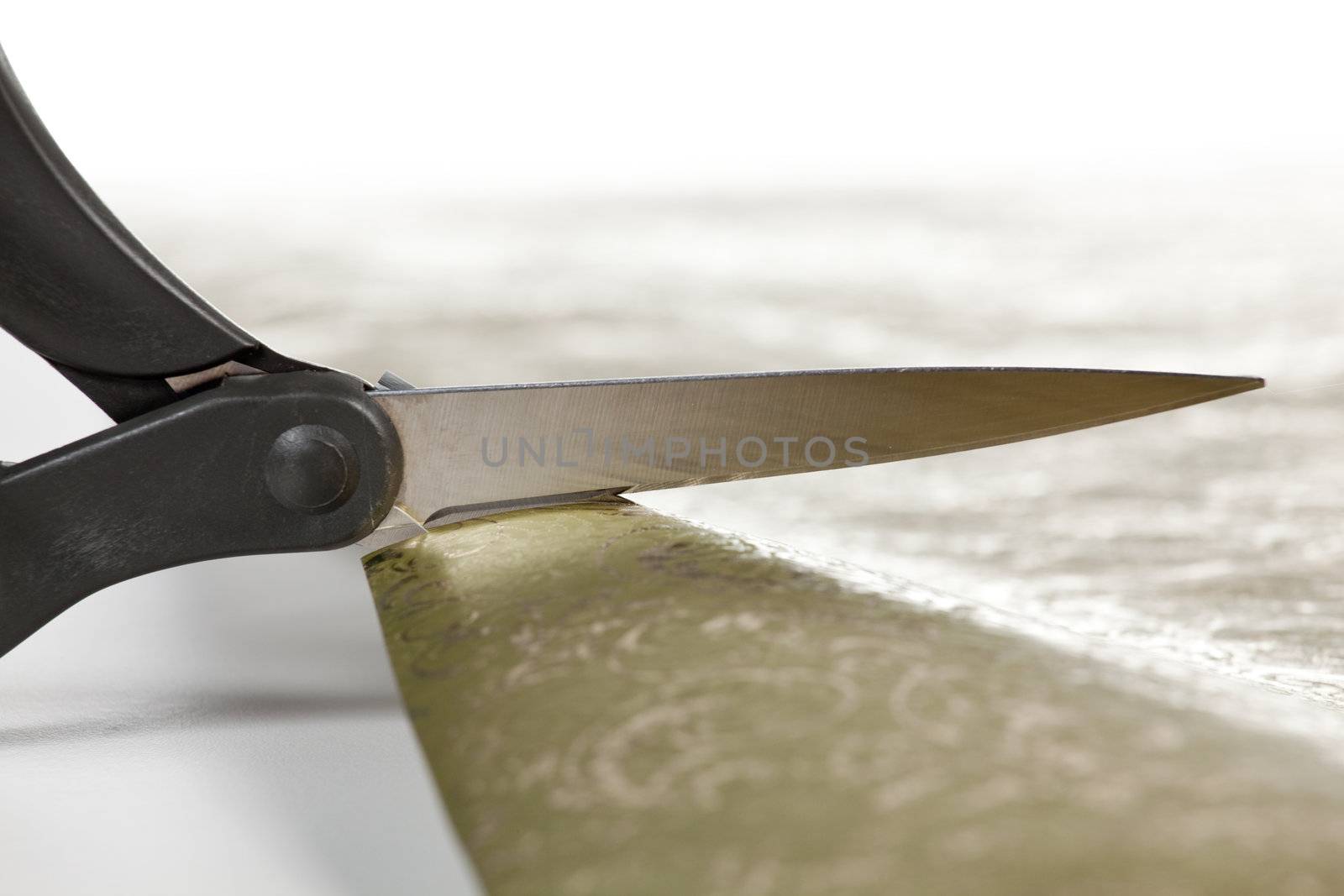 Close up of scissors cutting into gold colored christmas wrapping paper