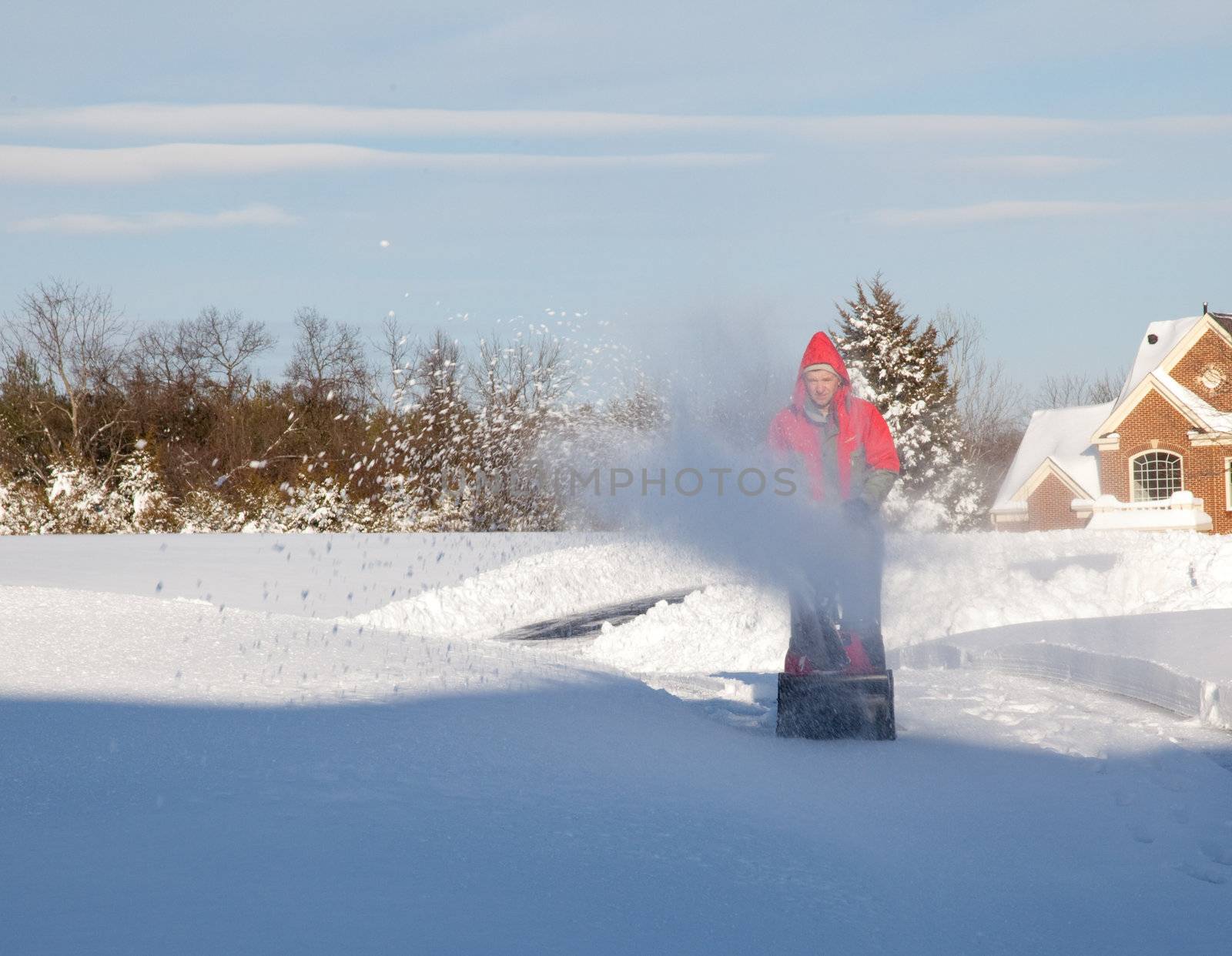 Senior man in red coat using a snow blower during a blizzard on home drive