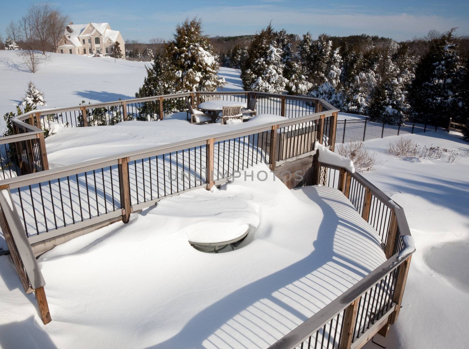Two tier deck covered with deep snow covering a small wooden table and chairs