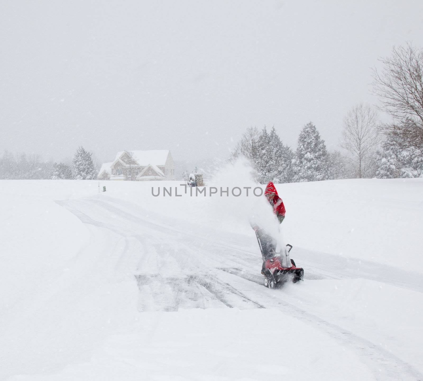 Senior man in red coat using a snow blower during a blizzard on home drive