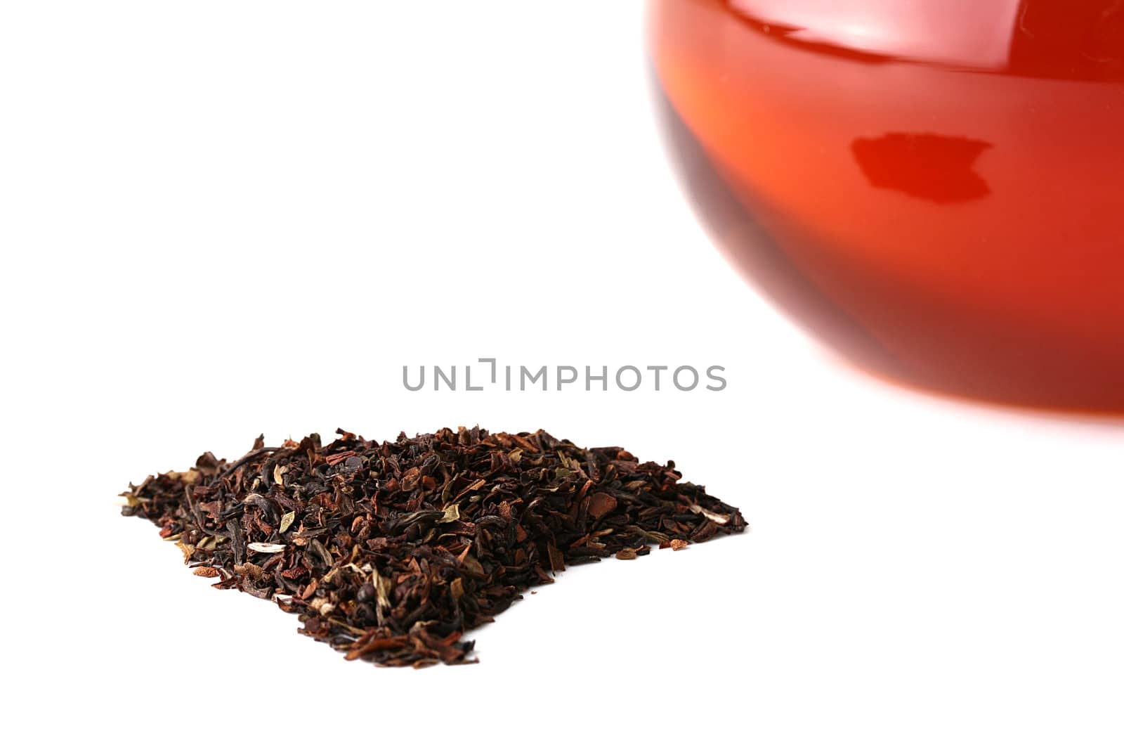 The dried up and crushed leaves of a tea-plant before a glass teapot for tea leaves.