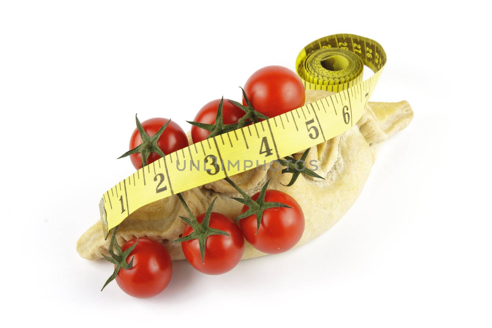 Contradiction between healthy food and junk food using tomatoes and a pasty with a tape measure on a reflective white background 