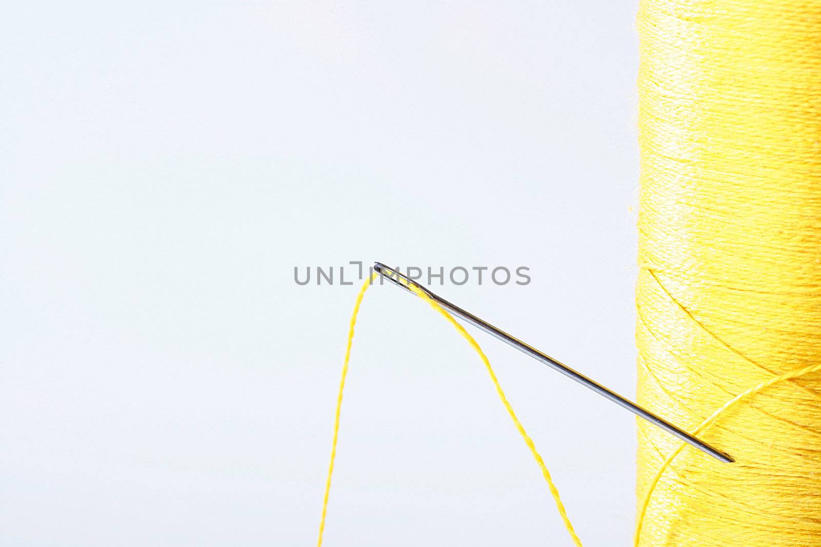 The coil of yellow threads with a needle for sewing.