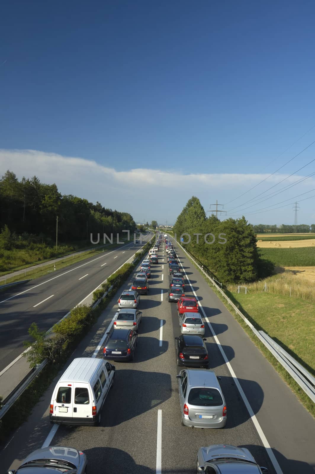 A line of stationary traffic stretches away into the distance on one side of the freeway (motorway, autoroute, autobahn) whilst, in the other direction it is completely clear.