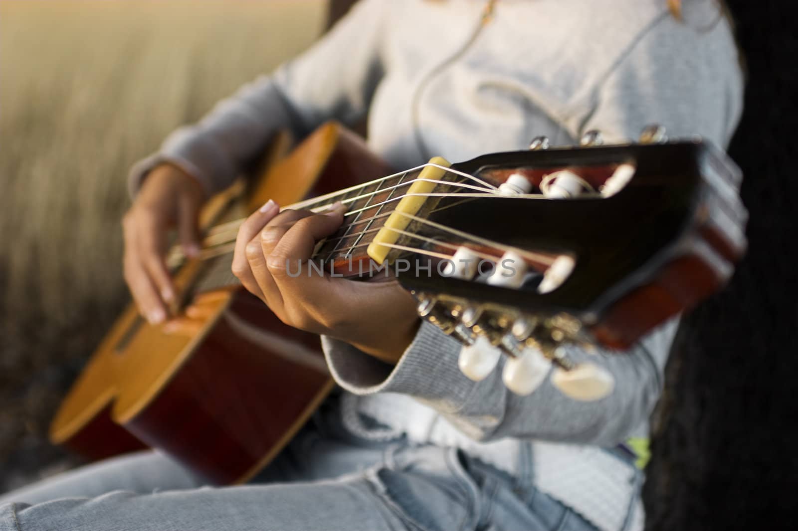 Woman playing her guitar at the sunset (focus is on the left hand) 