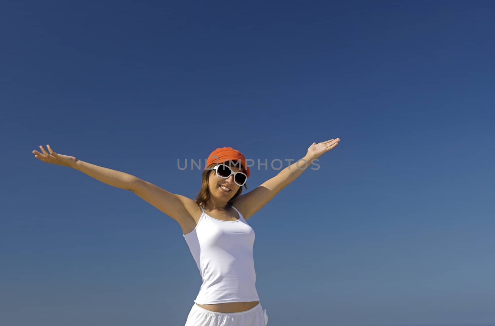 Happy woman with a orange hat and white glasses against a blue sky