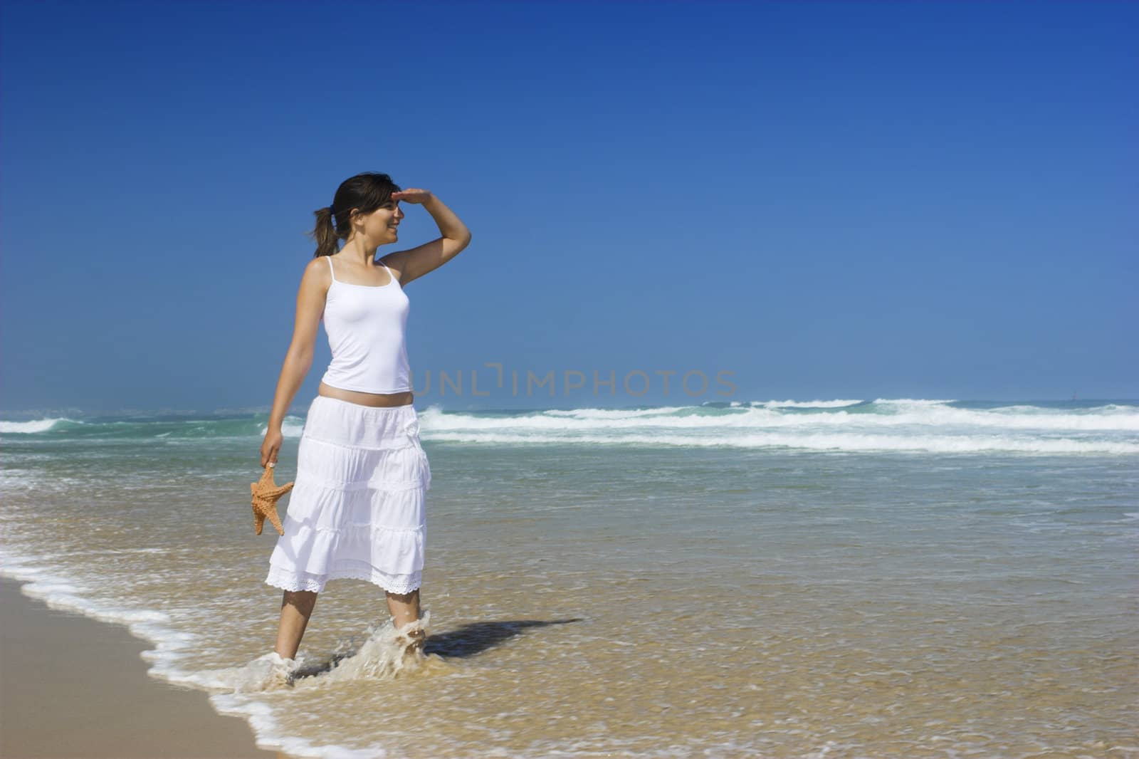 Beautiful woman on the beach with a starfish on the hand observing something