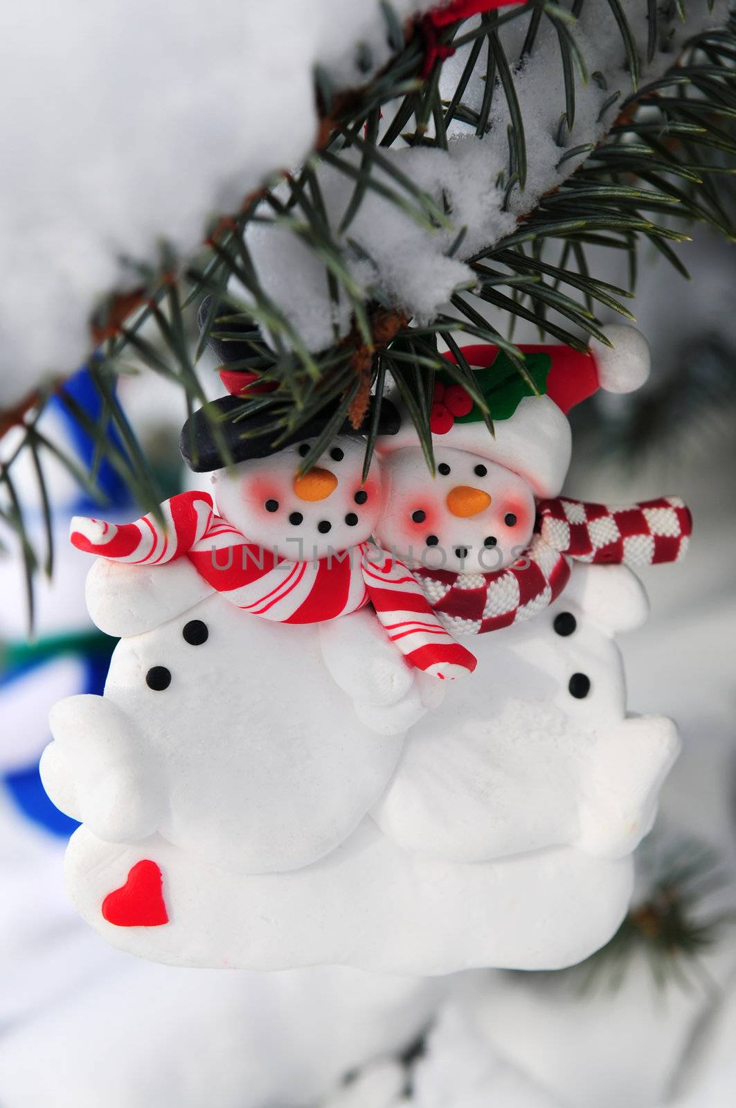 Snowmen Christmas ornament hanging on snow covered spruce tree outside