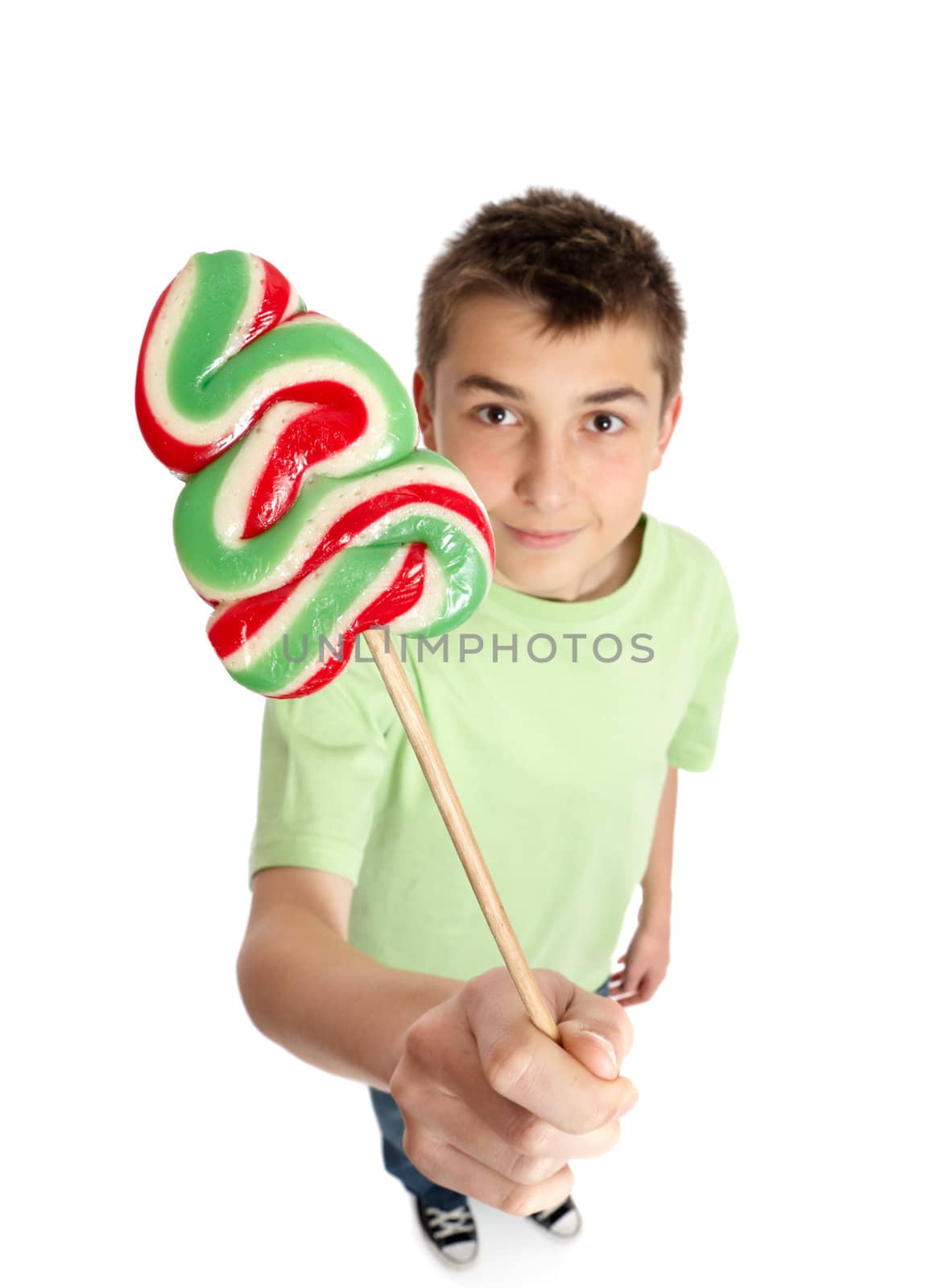 Boy holds our a Christmas tree lollipop on a stick - above view with focus to candy. Shadow under feet.