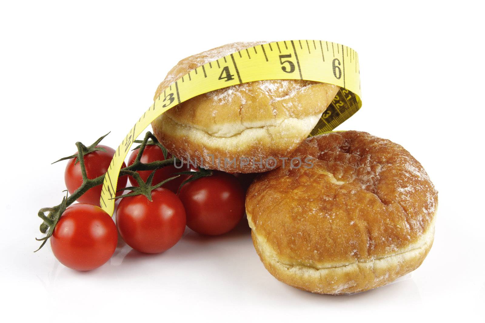 Contradiction between healthy food and junk food using red ripe tomatoes and doughnuts with a yellow tape measure on a reflective white background 