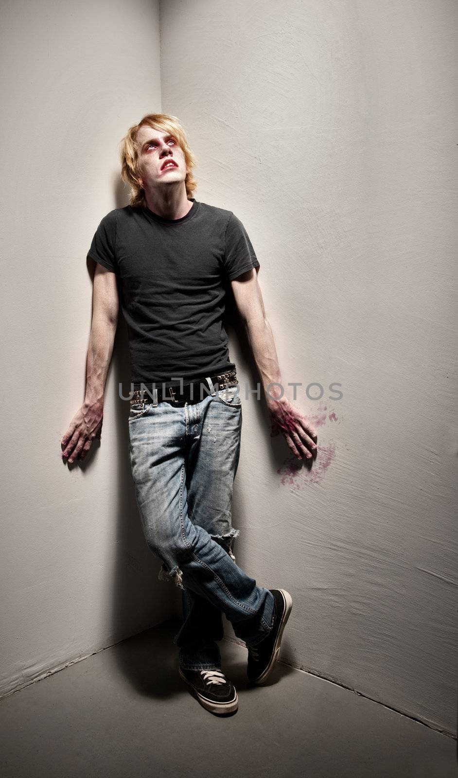 Young male zombie with bloody hands in corner
